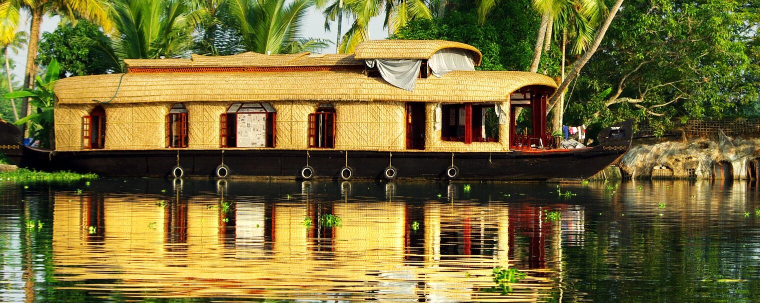 Converted rice barn (kettuvallam) floating on canal river, with exotic palm trees in the background